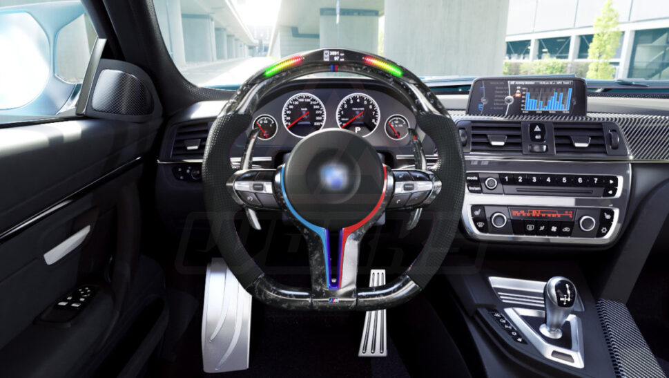 Front view of a BMW F chassis, M sport retrofit steering wheel in forged carbon fiber, extended paddle shifters, m color accents, black perforated leather, m color painted center trim, and led shift lights